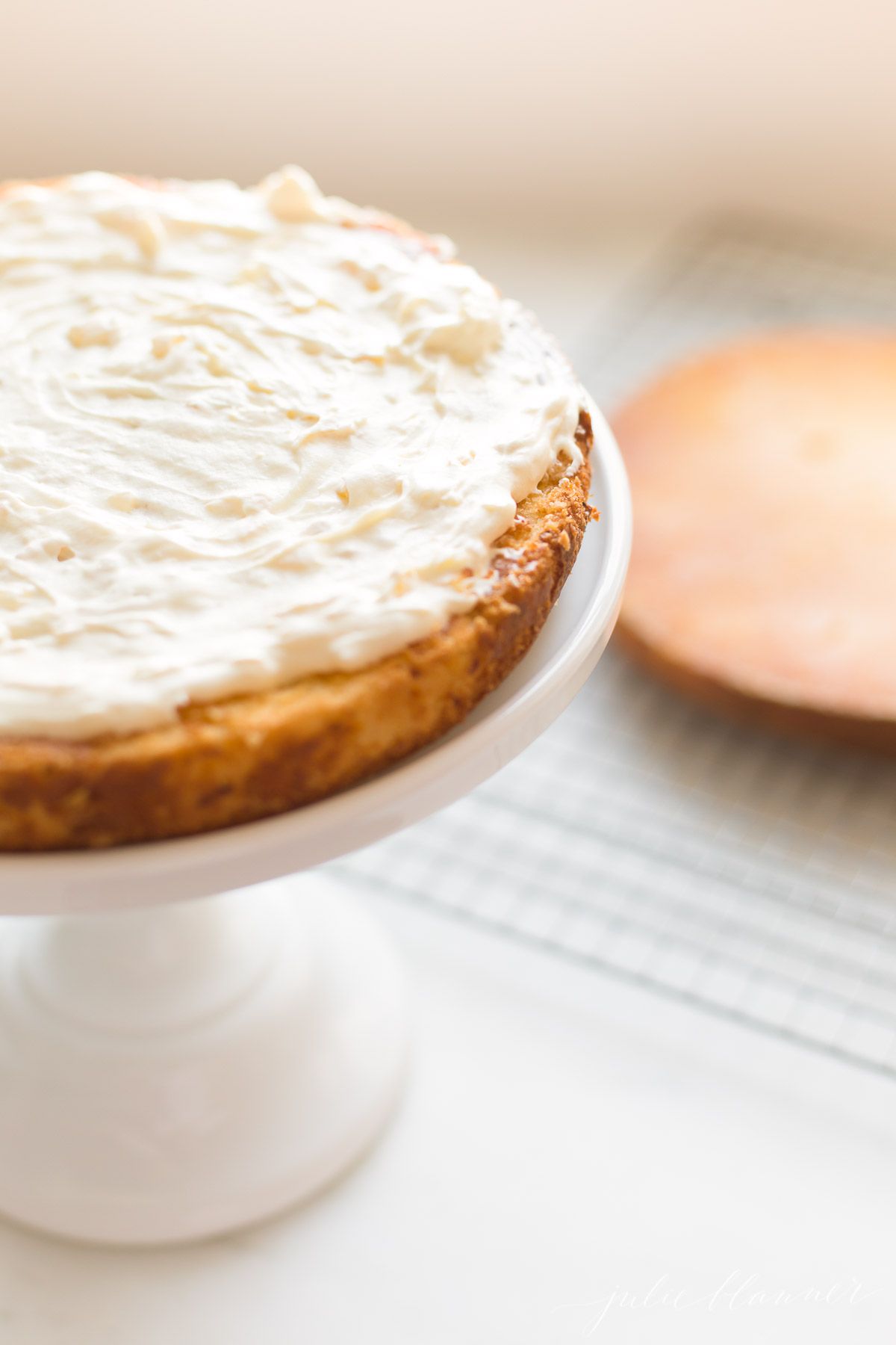 A round cake on a cake stand in the process of being frosted.