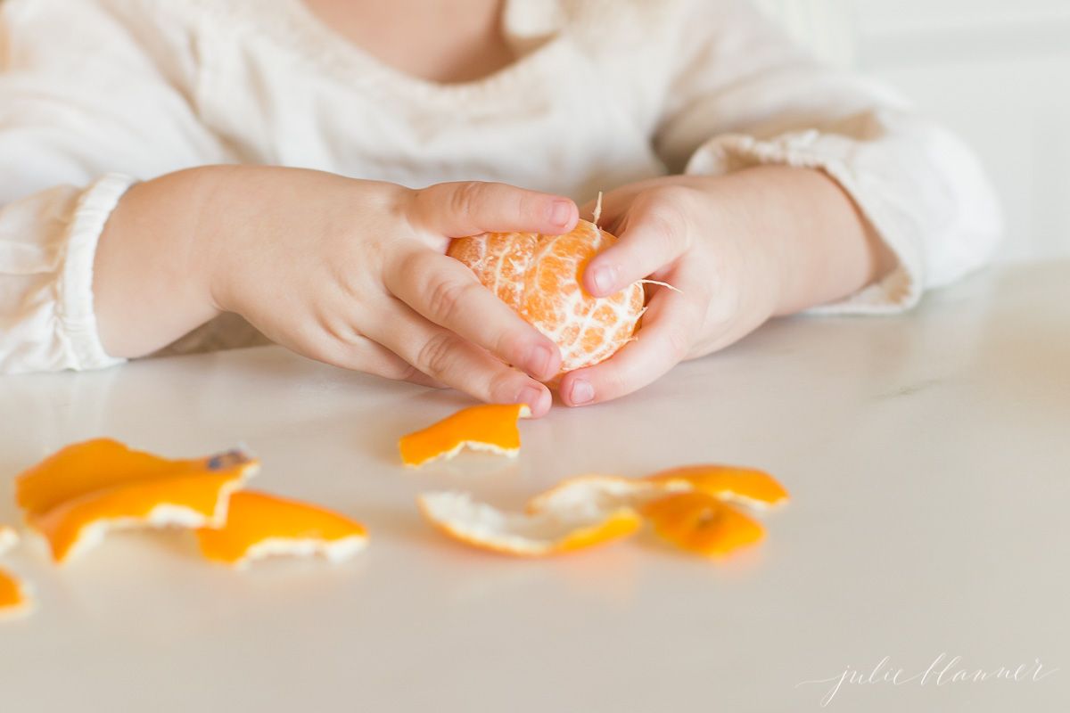 A child's hands peeling a mandarin orange.