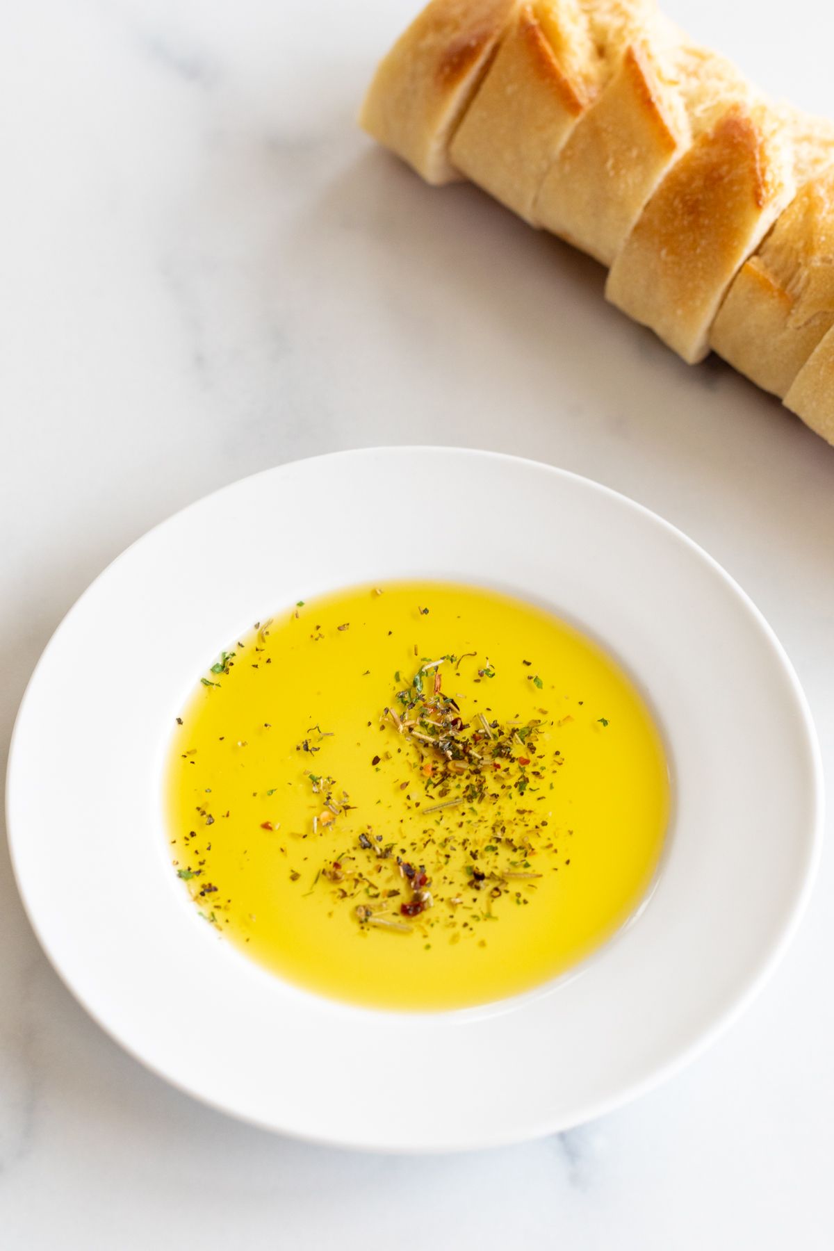 A white plate topped with bread dipping seasoning and olive oil, sliced bread in the background.