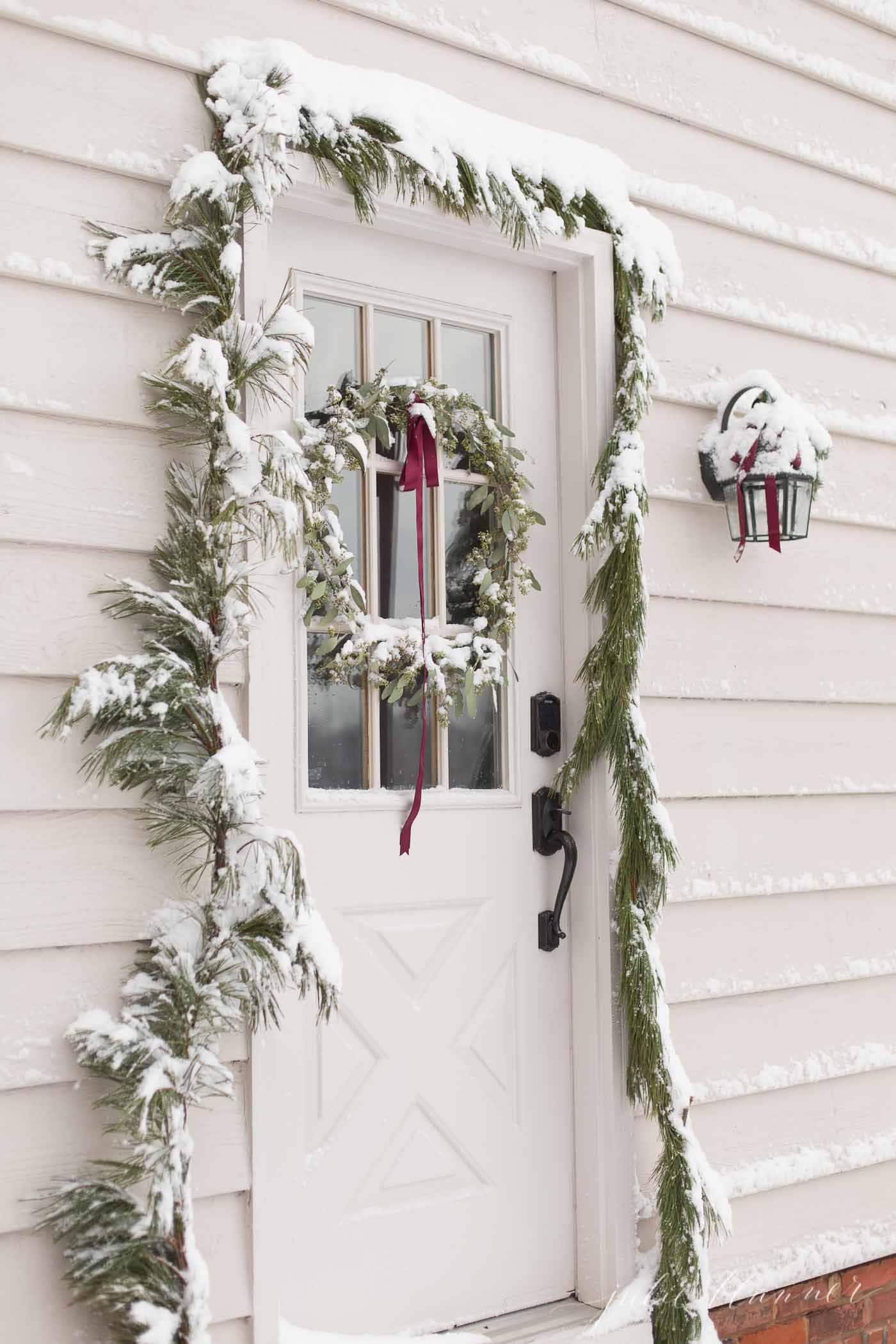 christmas door with a DIY wreath and garland covered in snow