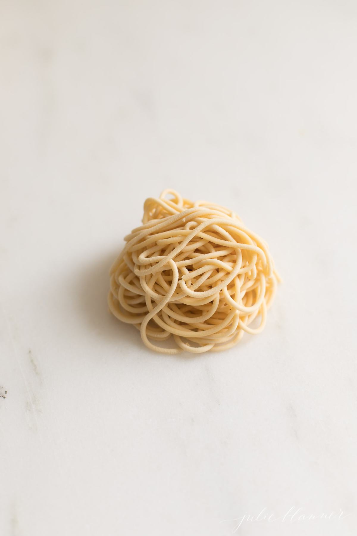 A little pile of homemade egg noodles in spaghetti shape on a marble countertop