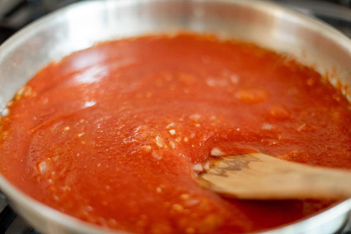 A tomato sauce cooking on a range, wooden spoon to the side.