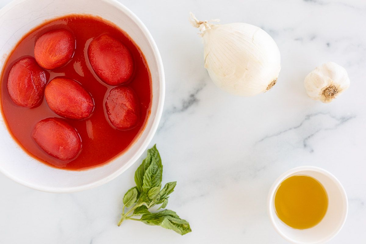 Ingredients for a pomodoro sauce recipe laid out on a marble surface.