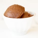 A small white bowl full of chocolate butter, on a marble surface.