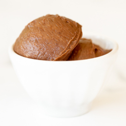 A small white bowl full of chocolate butter, on a marble surface.