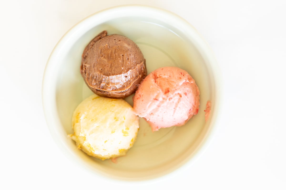 A small white bowl with a scoop of chocolate butter, strawberry butter and orange butter.