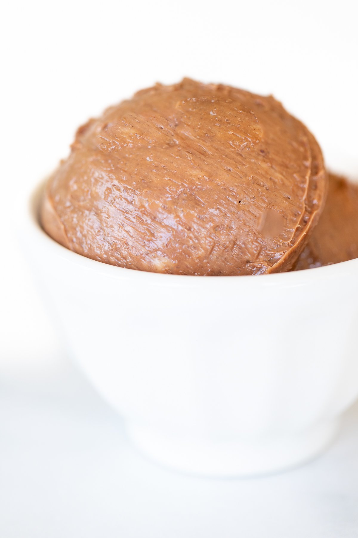 A small white bowl full of chocolate butter, on a marble surface.