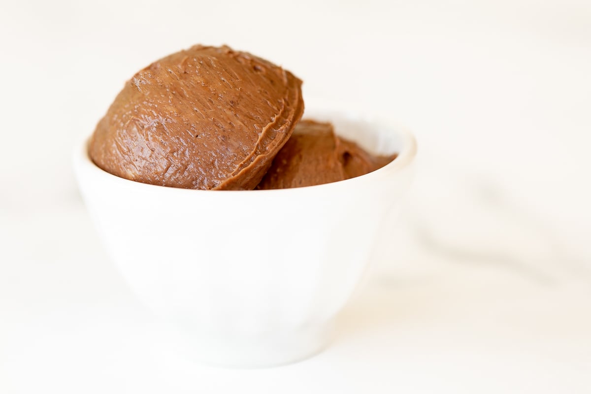 A small white bowl full of chocolate butter, on a marble surface.