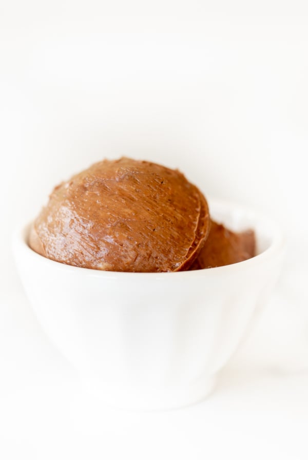 A small white bowl full of chocolate butter, on a marble surface.