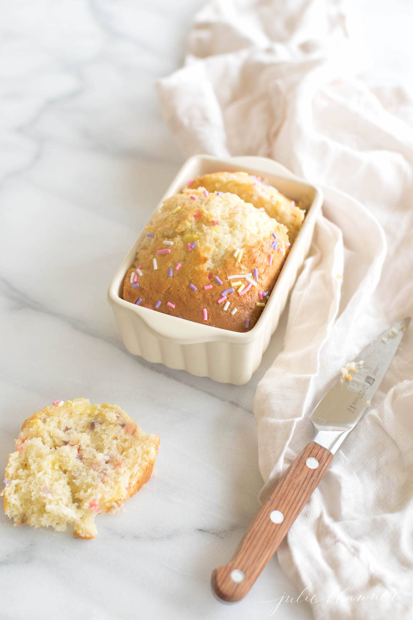 a small loaf of a funfetti bread recipe with a slice removed onto the marble countertop