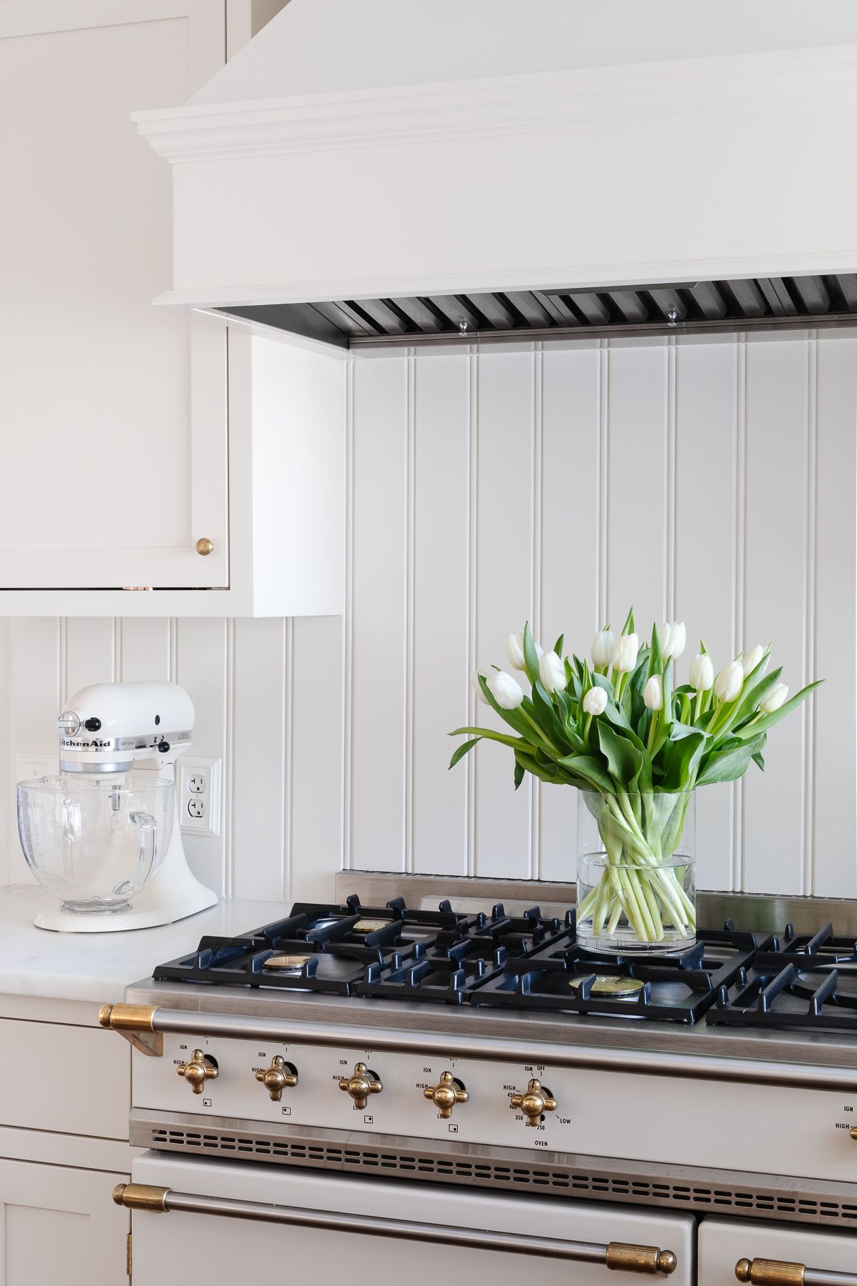 A cream kitchen wit ha tulip arrangement in a glass vase, resting on an ivory and brass French range.