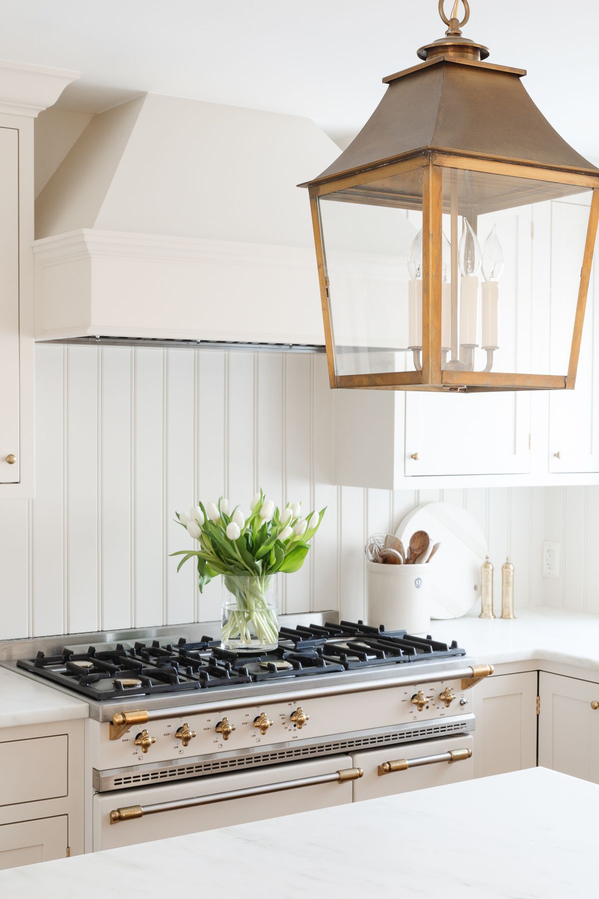 A cream kitchen wit ha tulip arrangement in a glass vase, resting on an ivory and brass French range.