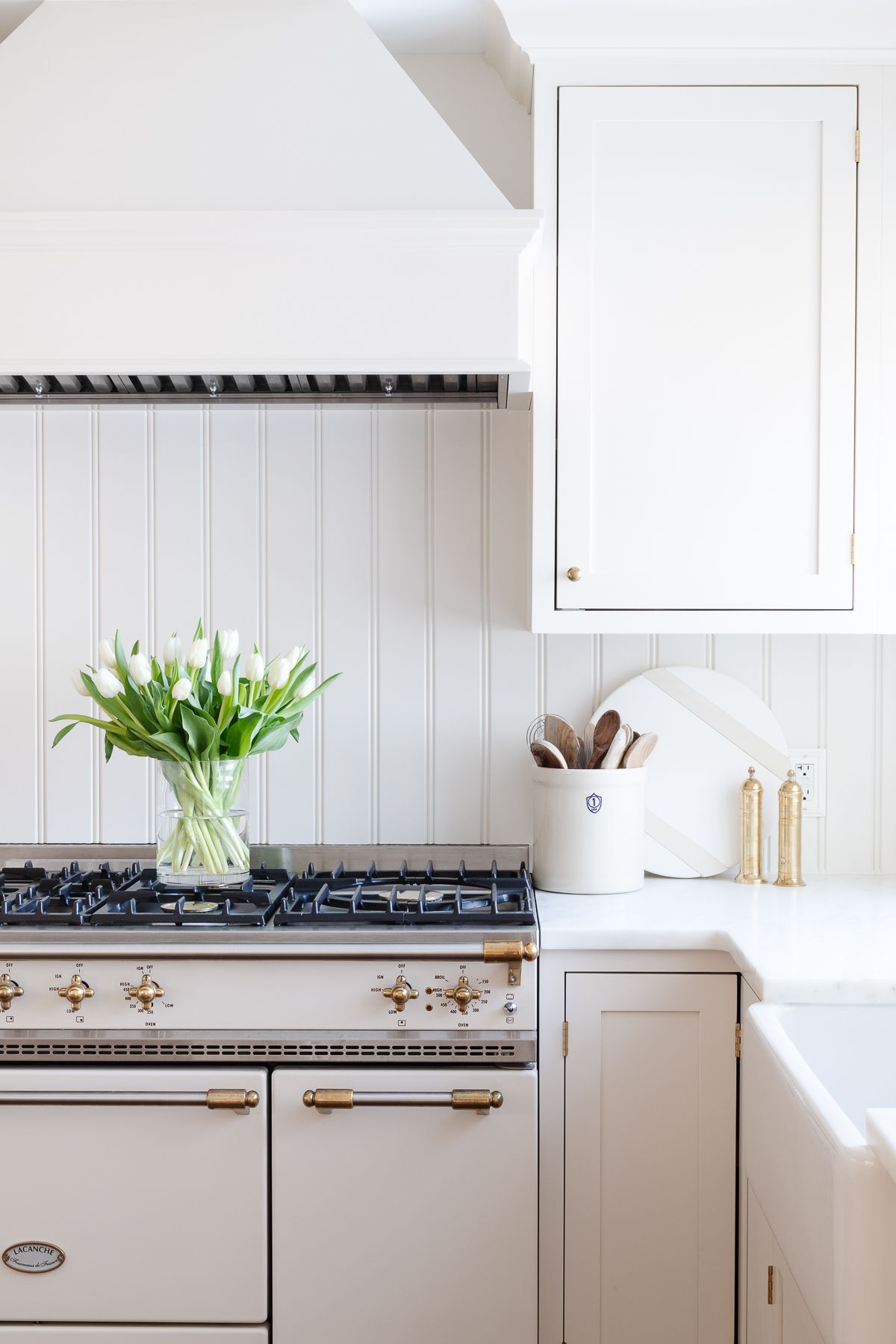 A cream kitchen wit ha tulip arrangement in a glass vase, resting on an ivory and brass French range.