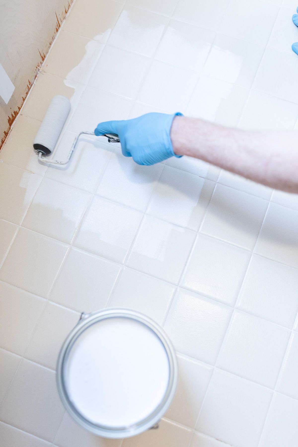 A person in latex gloves rolling primer onto old bathroom tiles