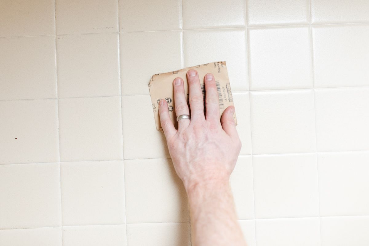 A hand sanding old tile with a sanding block