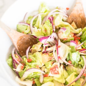 Fresh Italian garden salad with sliced red onions and wooden serving utensils.