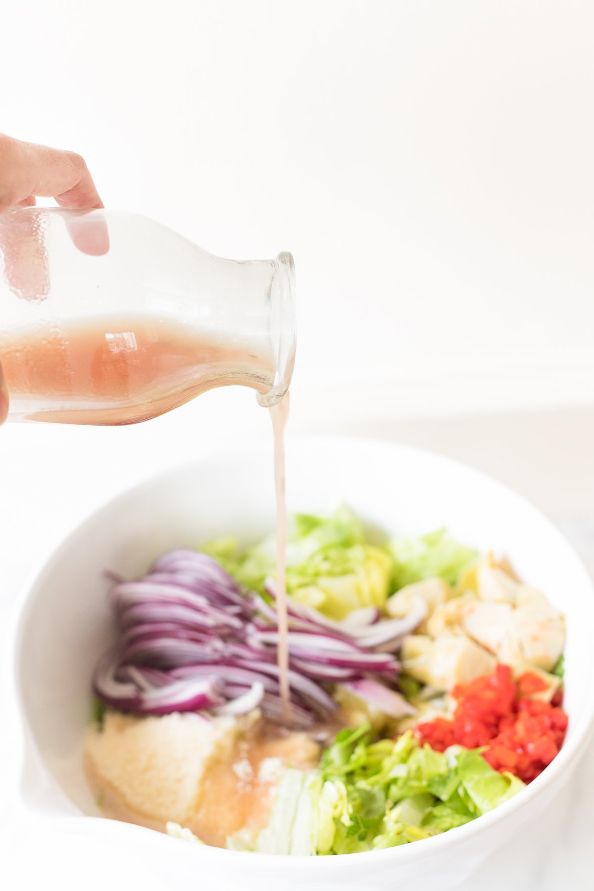 Dressing being poured onto a fresh Italian garden salad with chicken.