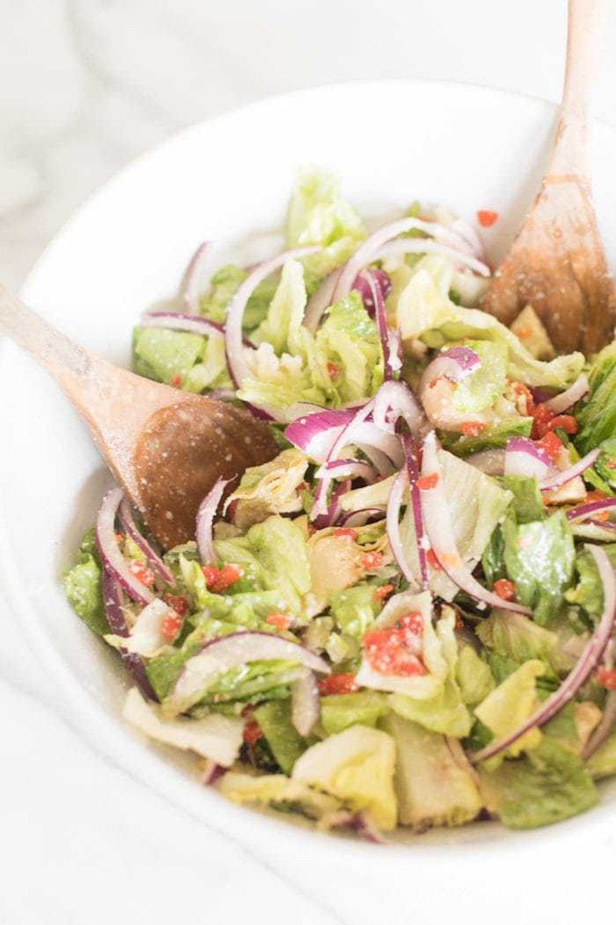 A white bowl full of Italian salad, with wooden spoons.