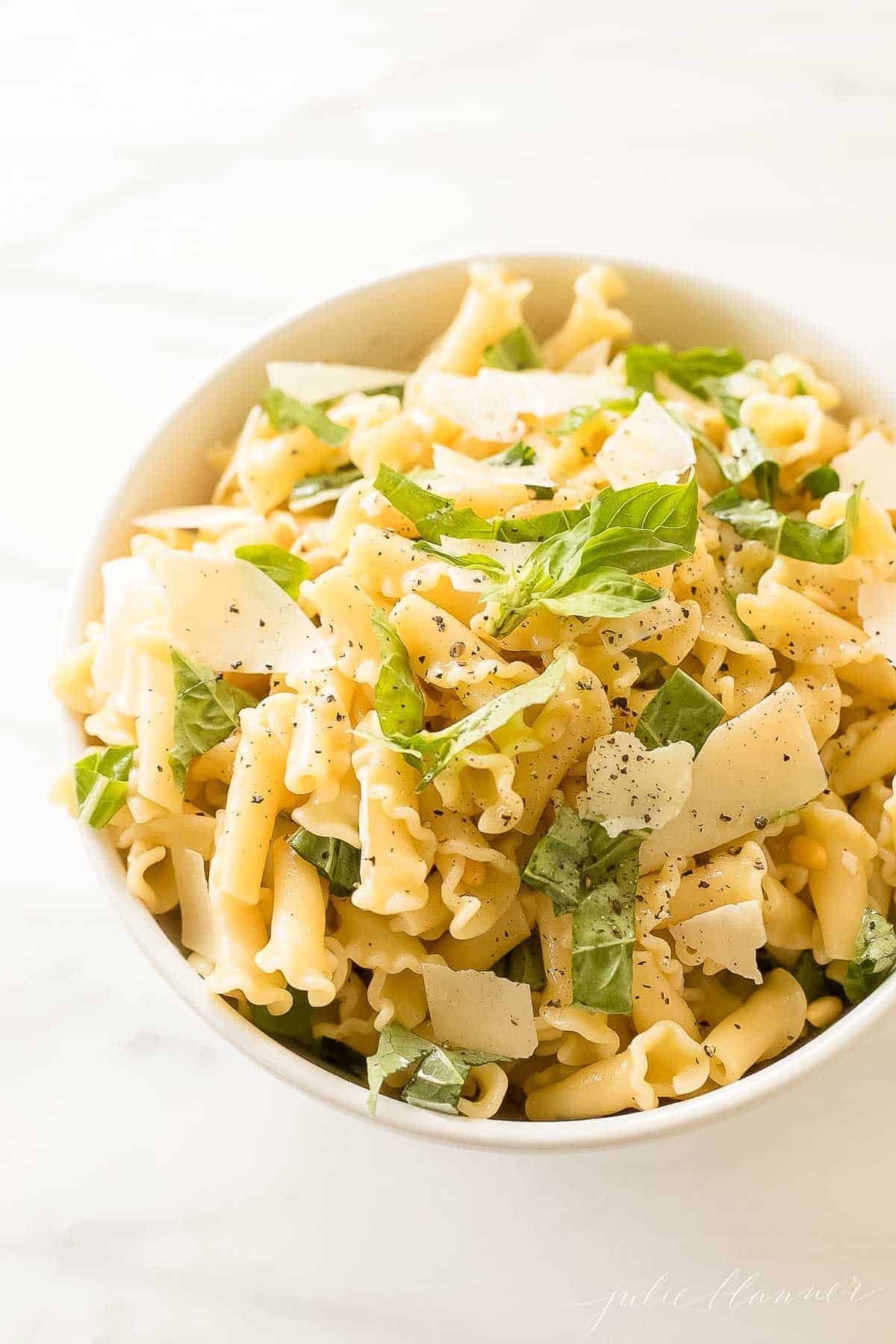 pasta topped with parmesan and basil in white bowl