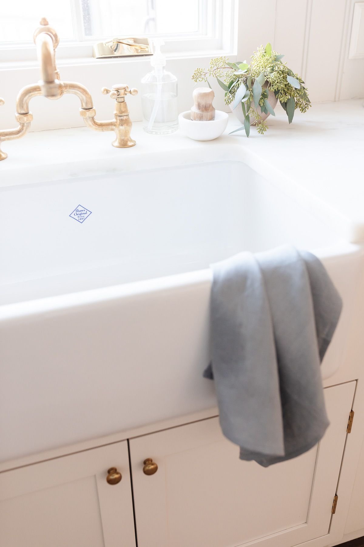 A kitchen farm sink with a brass faucet and linen towel draped over the front