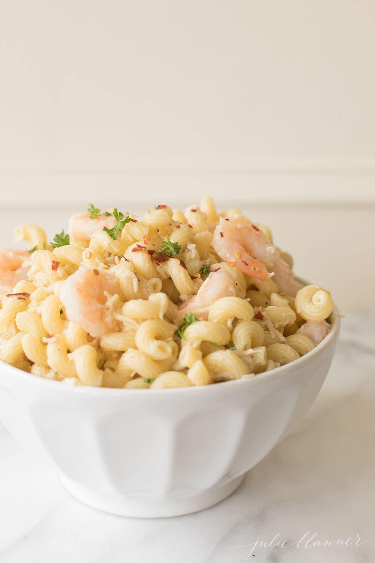 A white bowl of seafood pasta salad on a marble surface. 