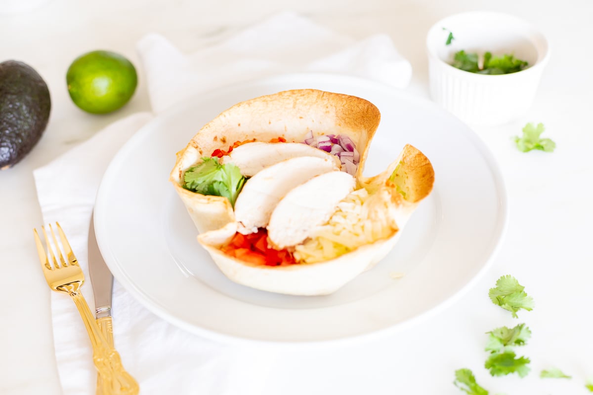 taco salad in tortilla bowl with gold utensils