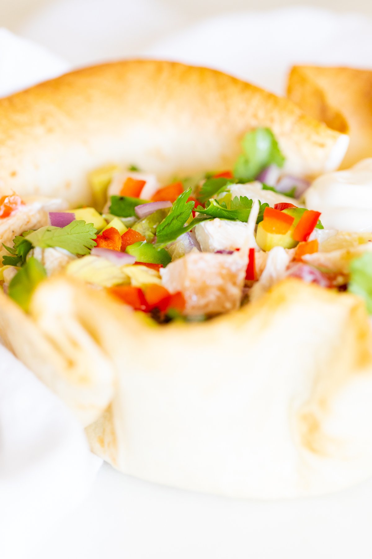 A chicken taco salad in a homemade tortilla bowl on a white plate.