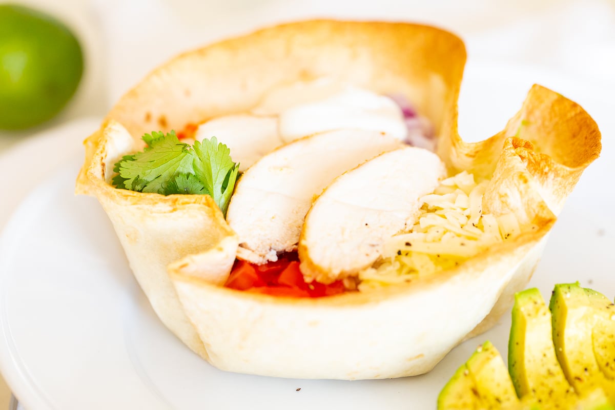 A chicken taco salad in a homemade tortilla bowl on a white plate.