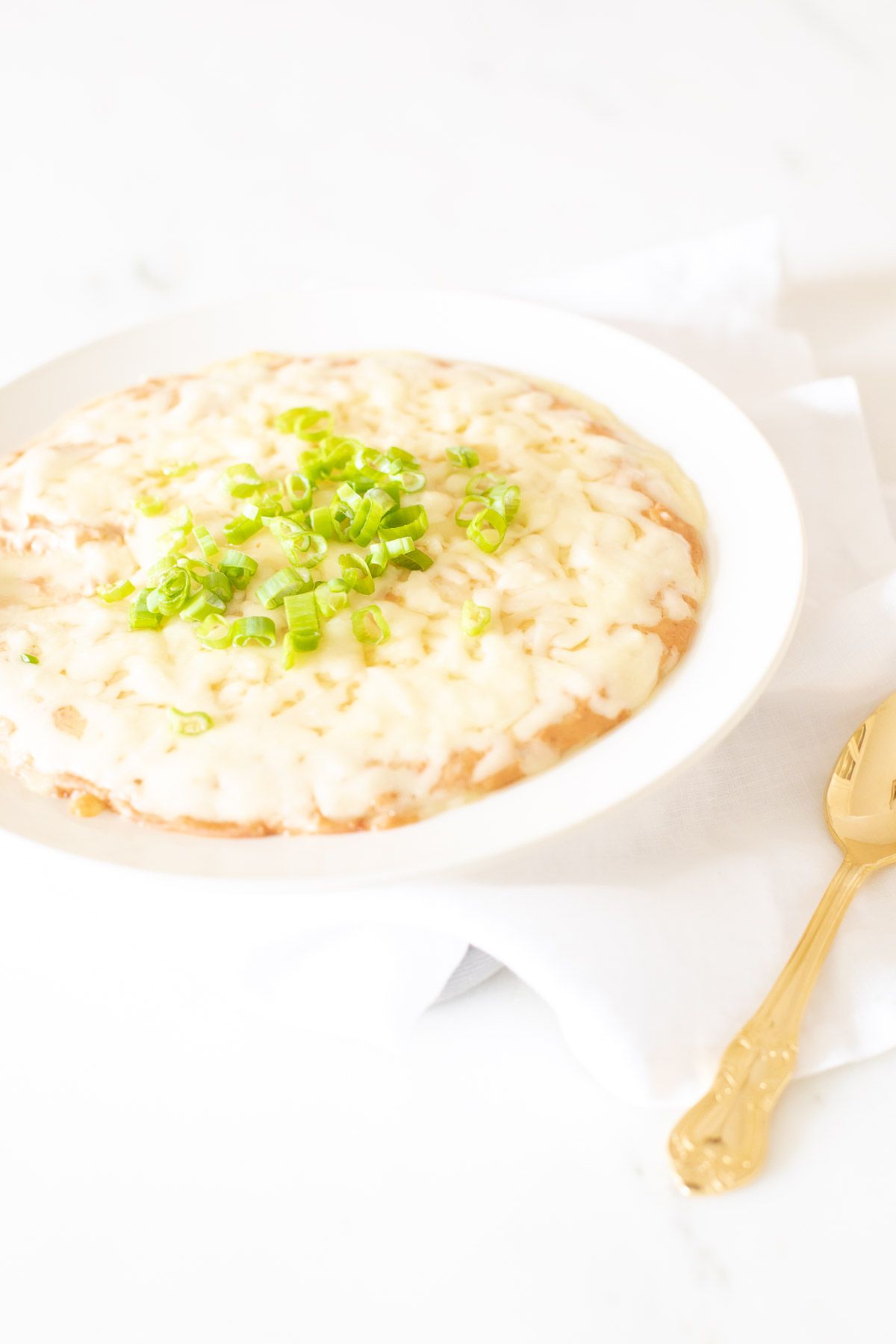 A white bowl full of cream cheese bean dip, topped with diced chives and gold spoon to the side