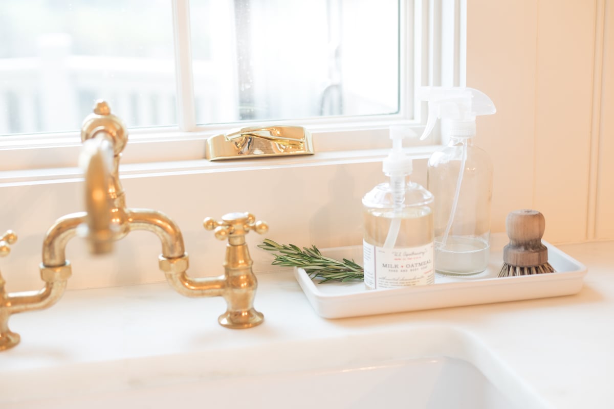 A sink with a tray of marble cleaner and a window.