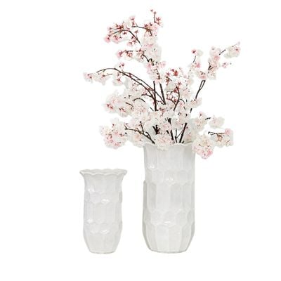 a pair of white honeycomb patterned flower vases with cherry blossom branches in one.