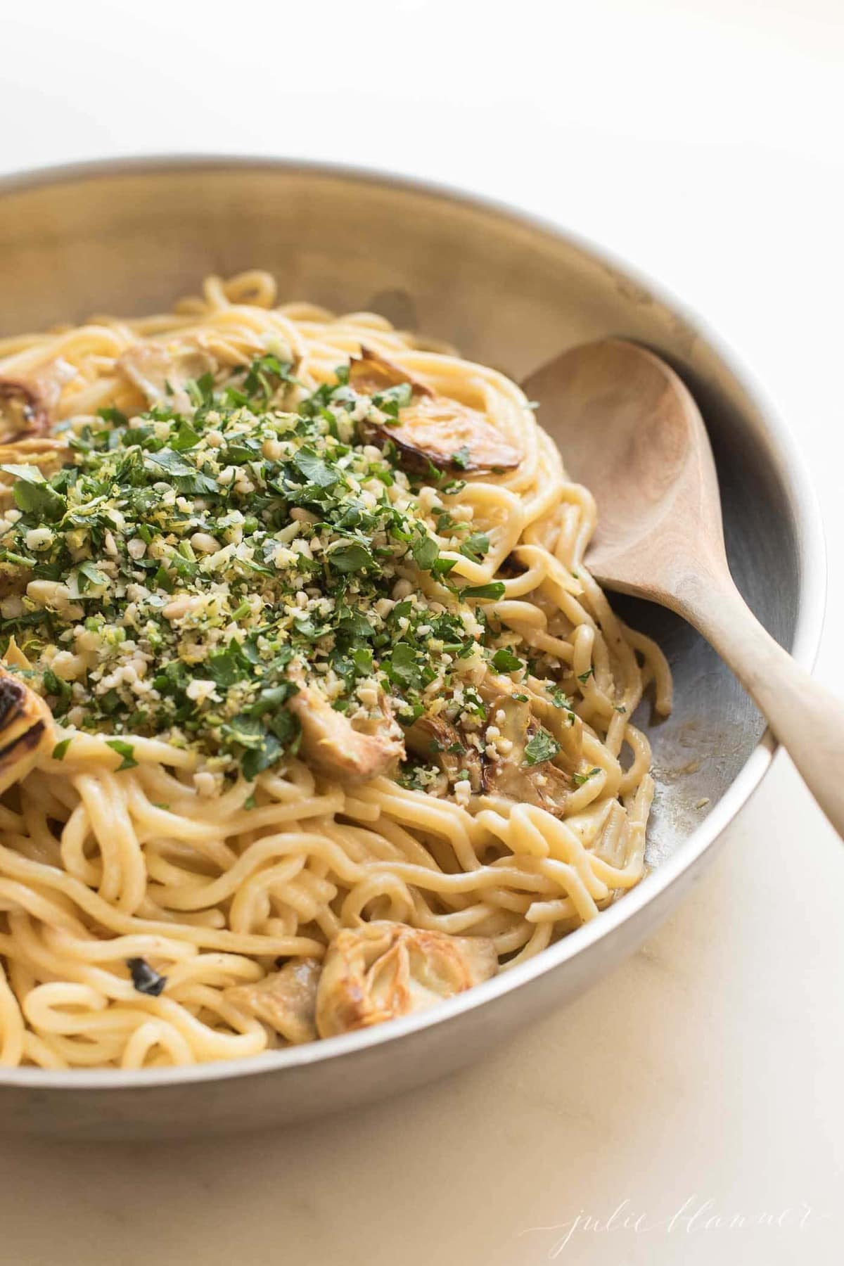 spaghetti in a skillet with artichokes and gremolata with a wooden spoon
