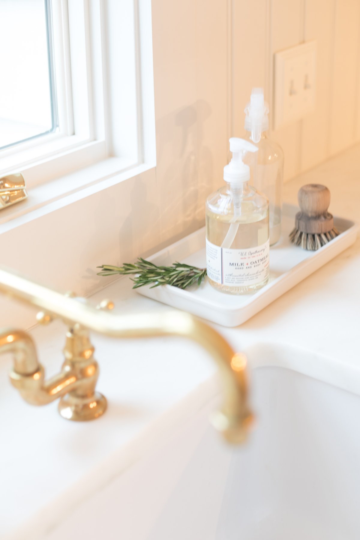 A white sink with a tray of marble cleaner and a gold faucet.