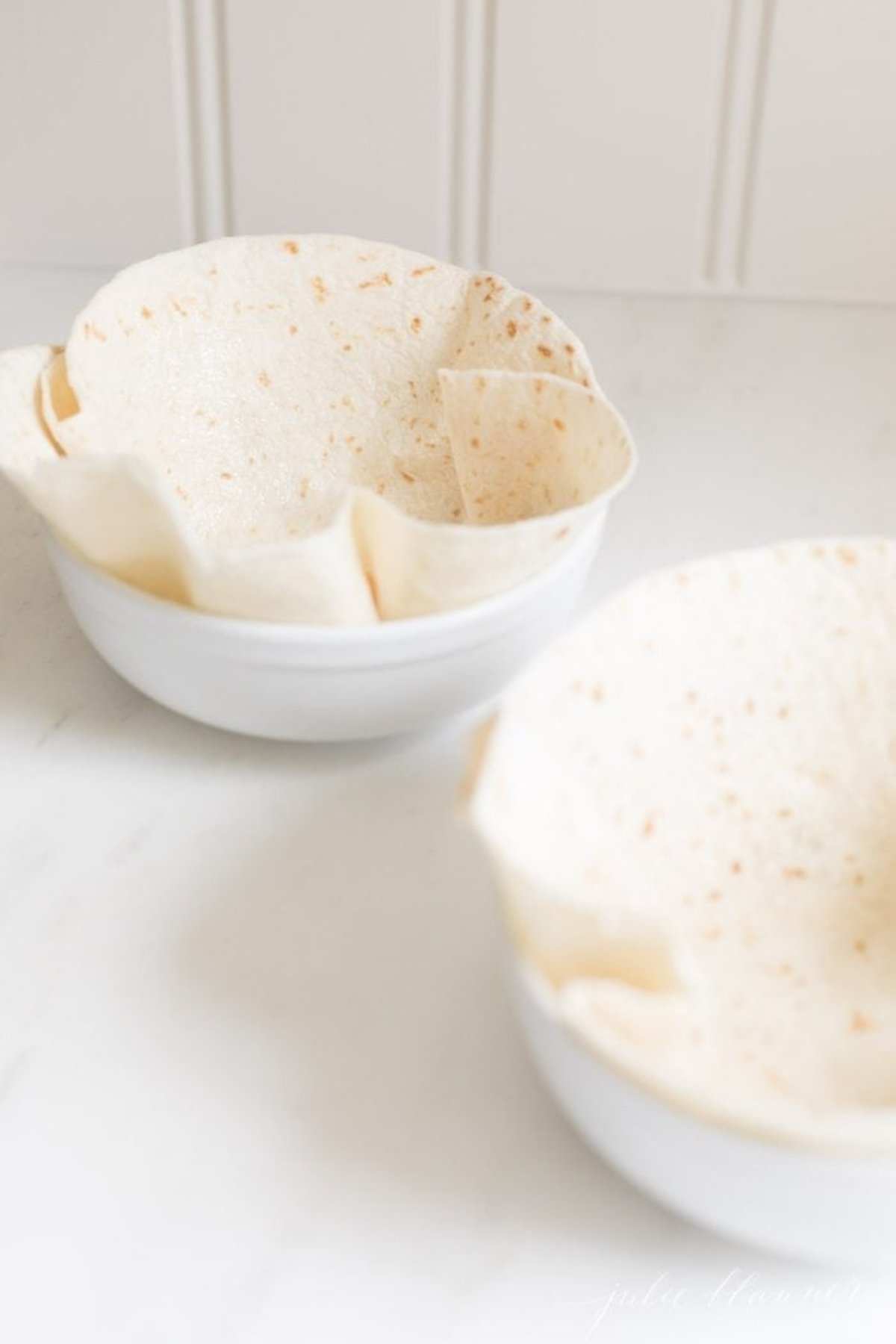 Two bowls with tortillas folded into them to bake into taco salad bowls.