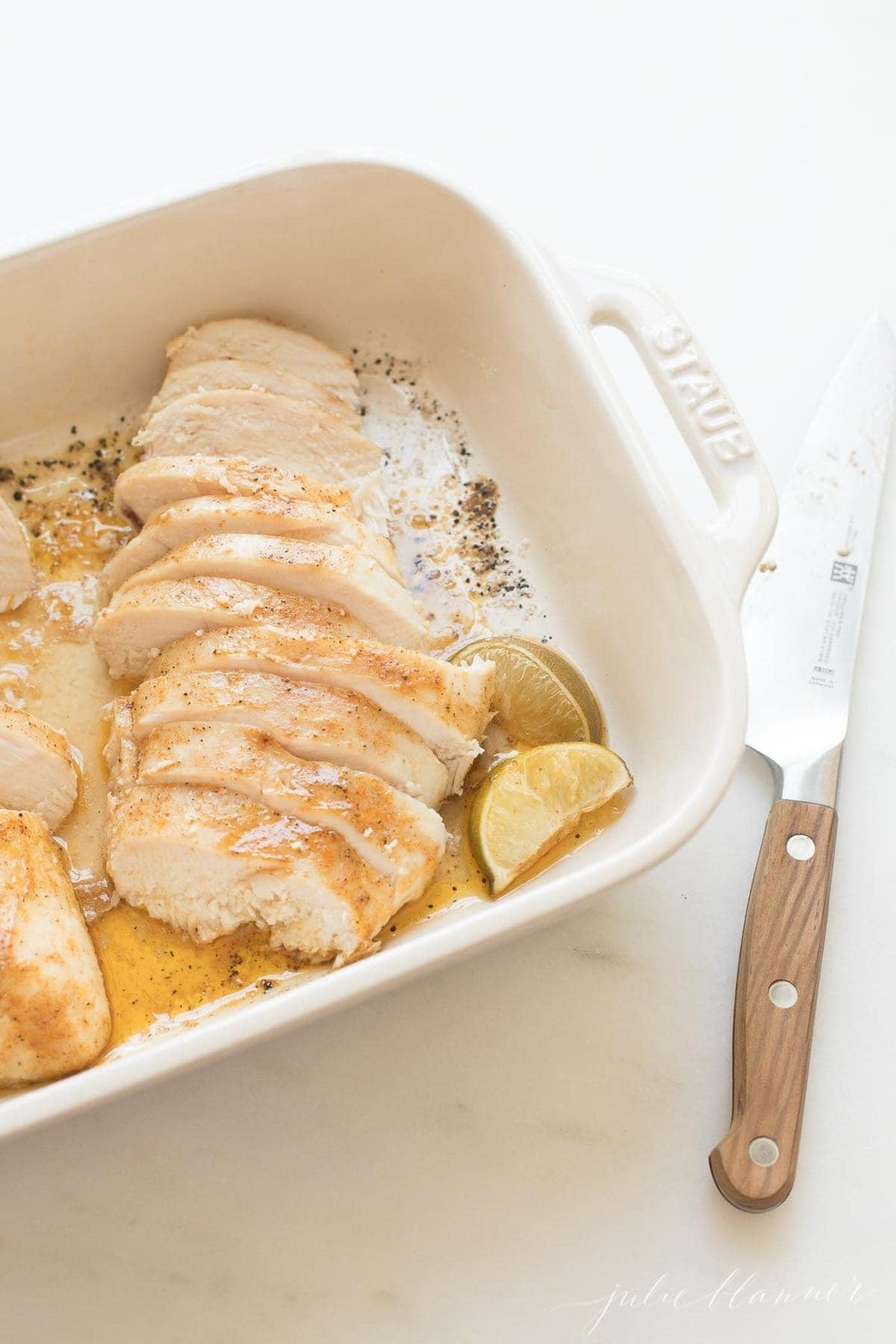 oven baked chicken breast sliced in a white baking dish. 