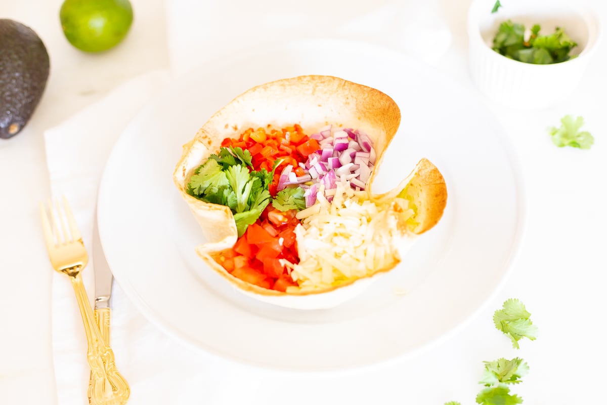 taco salad in tortilla bowl with gold utensils