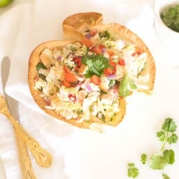 A chicken taco salad on a white surface, gold silverware and cilantro to the side.