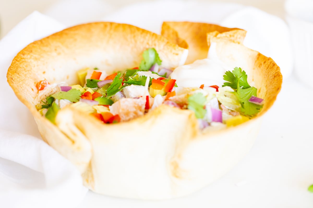 A chicken taco salad in a homemade tortilla bowl on a white plate.