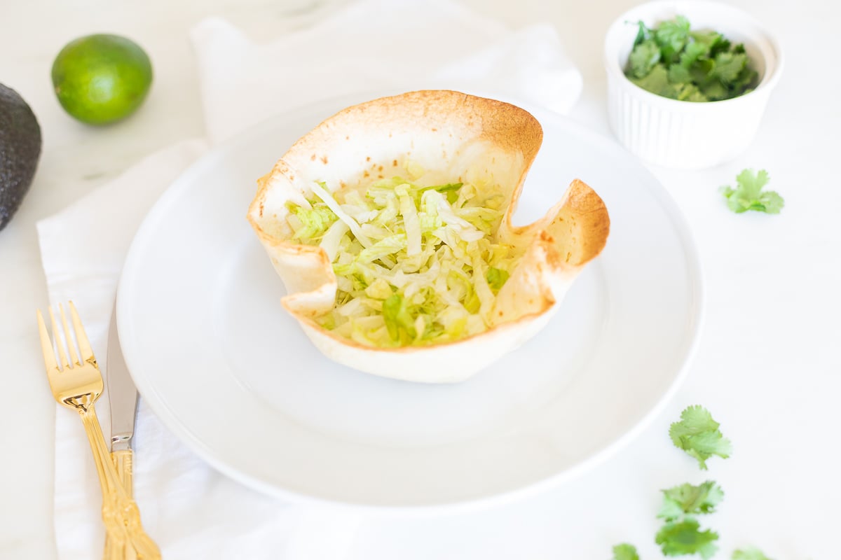 taco salad in tortilla bowl with gold utensils