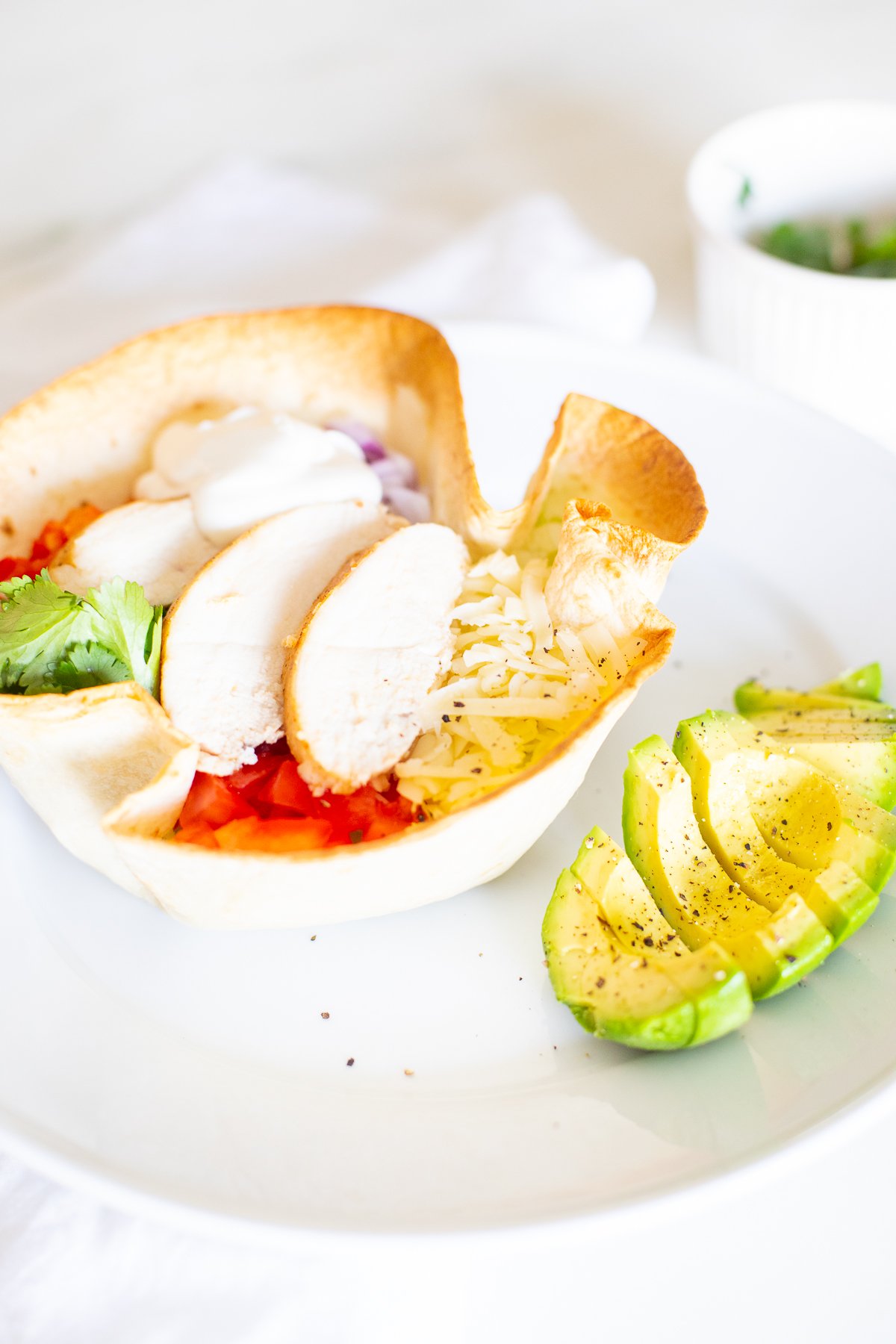 A chicken taco salad in a homemade tortilla bowl on a white plate.