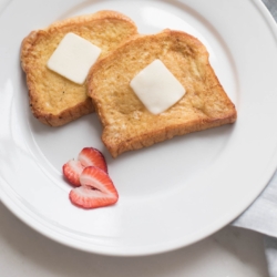 brioche french toast on a white plate, topped with butter.