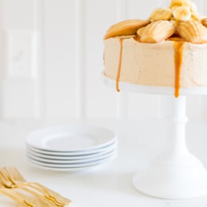 A round banana cake topped with madeleine cookies and caramel sauce.