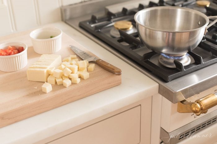 Diced white cheese on a cutting board with pot on the stovetop