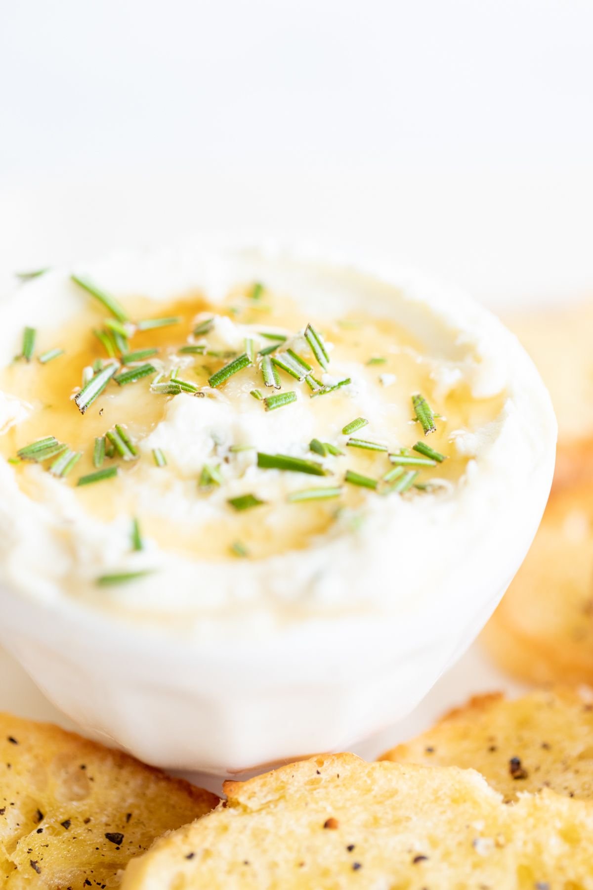 Whipped goat cheese with honey in a white bowl, on a platter of crostini for dipping.