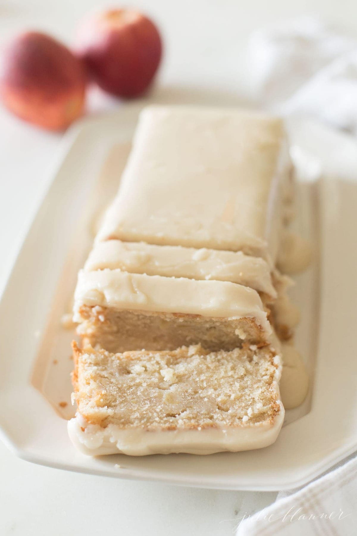 apple pound cake on a white platter, apples in background.