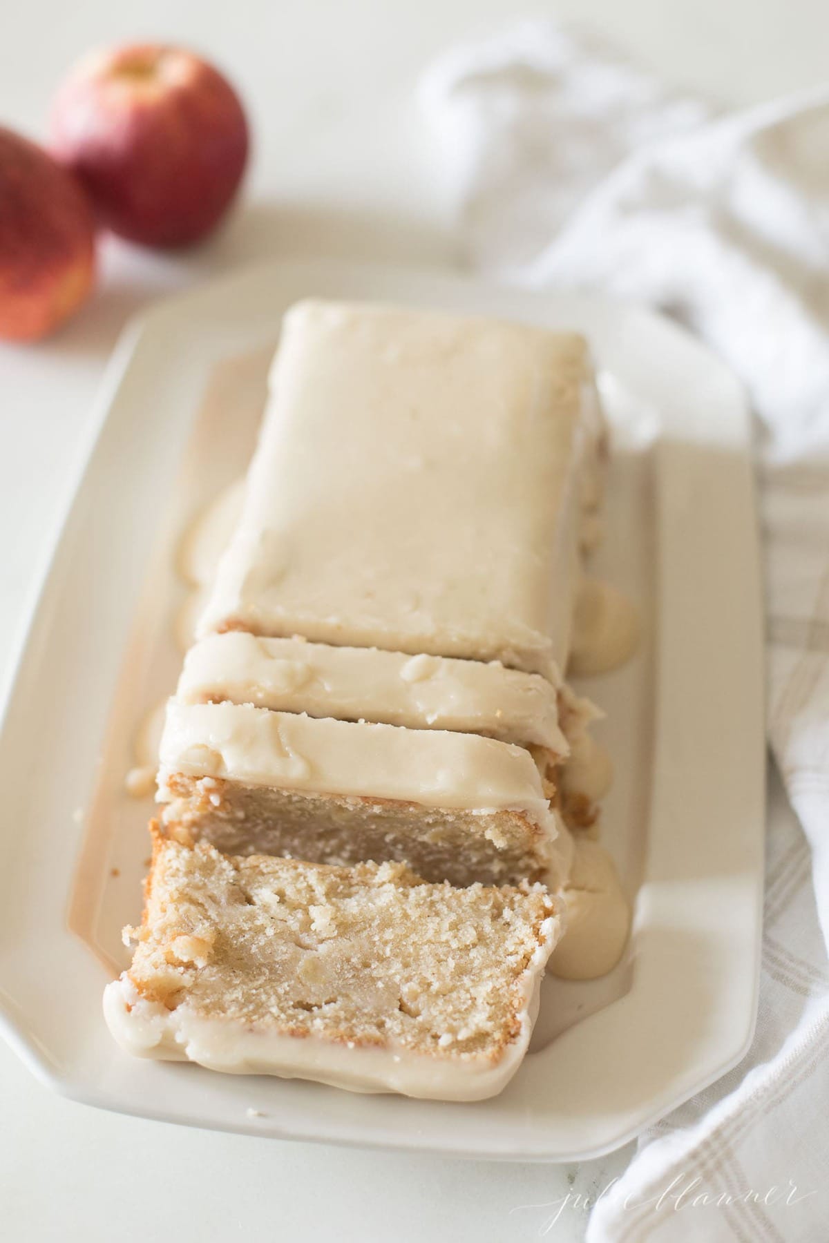 apple pound cake on a white platter, apples in background.