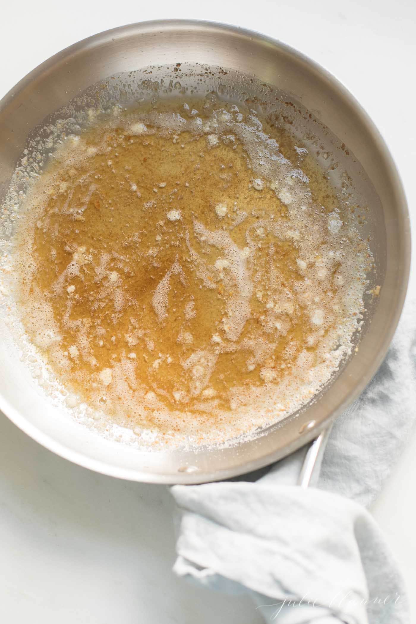 A silver pan with handle, warm browned butter inside, showing how to brown butter.