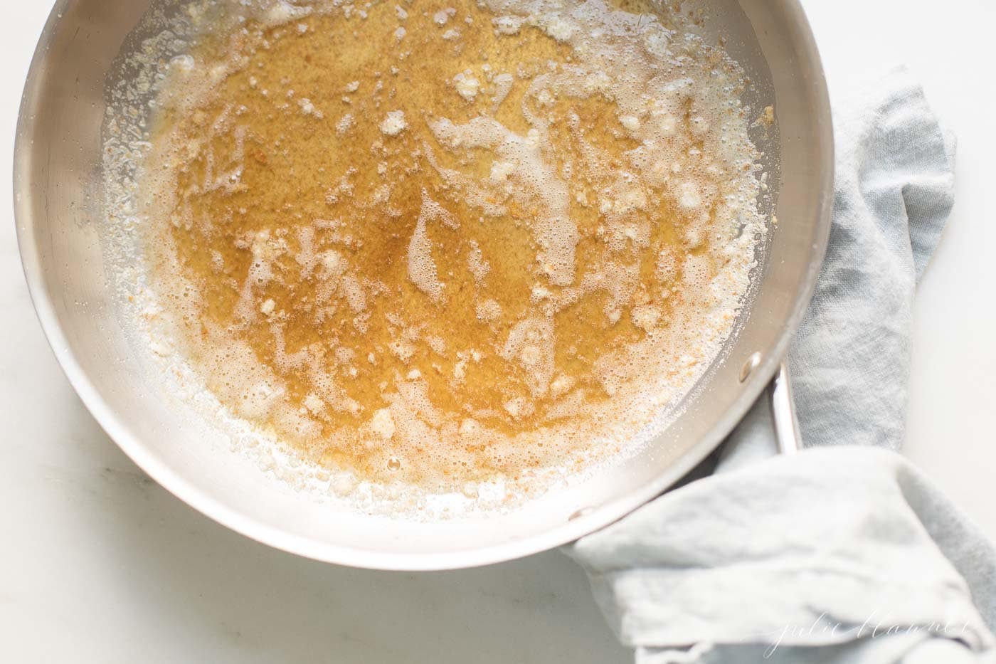 A silver pan with handle, warm browned butter inside, showing how to brown butter.