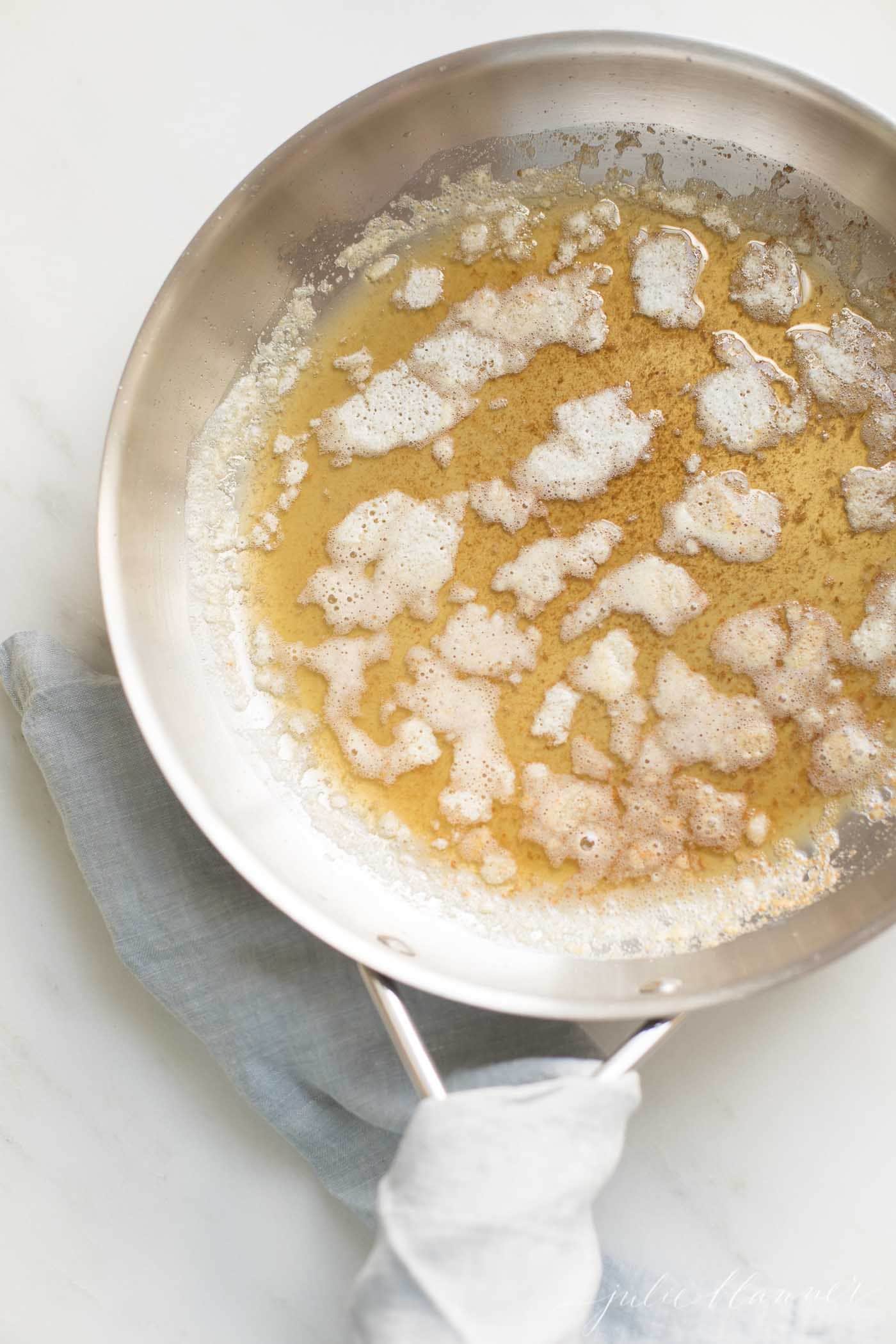 A silver pan with handle, warm browned butter inside, showing how to brown butter.