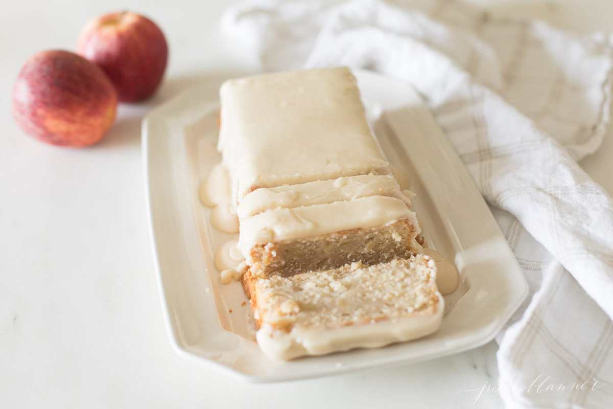 apple pound cake recipe on a white platter, apples in background.